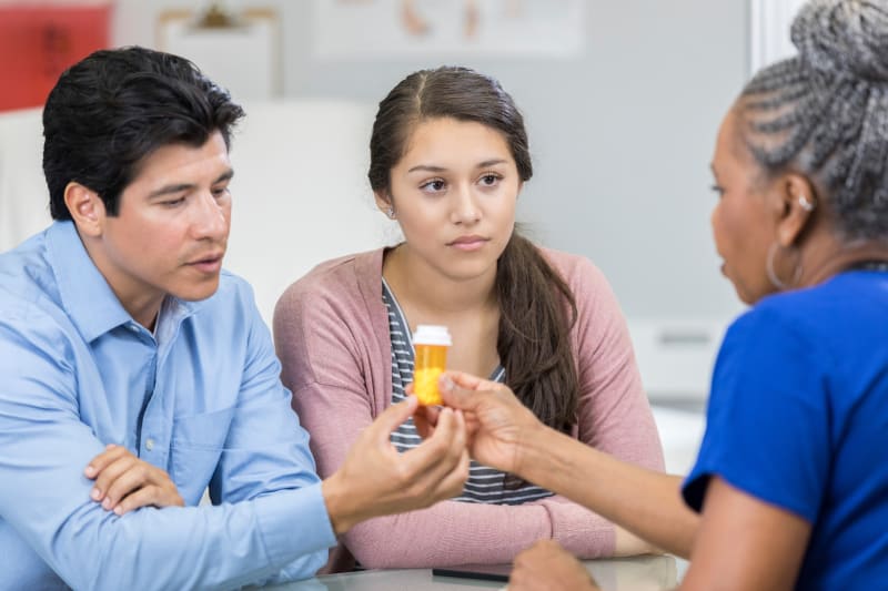 Doctor speaking with teenage girl and her father about prescription medication.