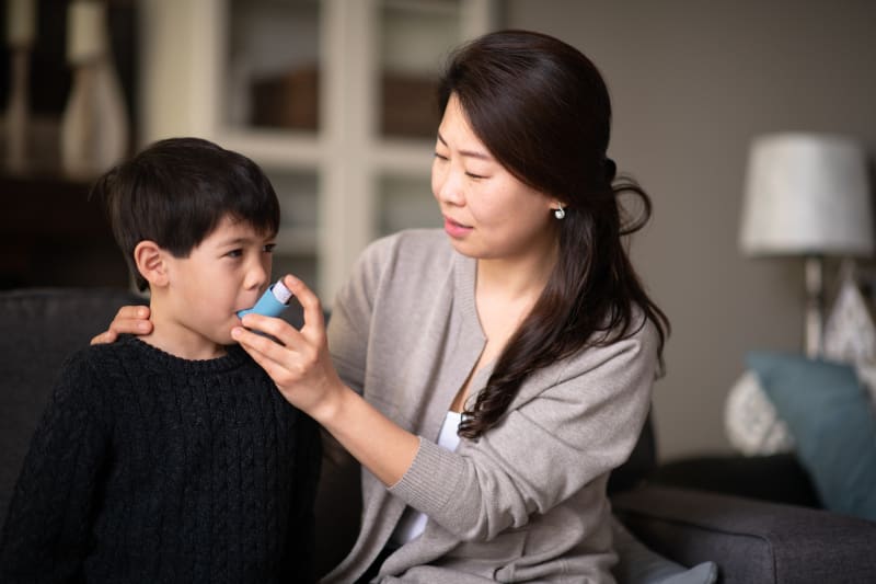 Mother helping son use asthma inhaler.