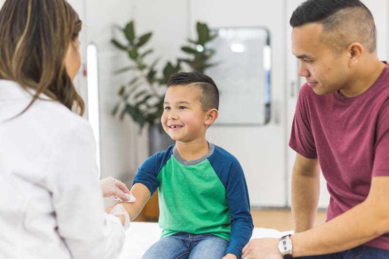 Young boy sitting with Dad at doctor's office while having blood drawn.