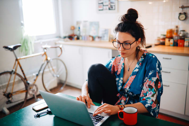 Young woman using laptop at kitchen table.