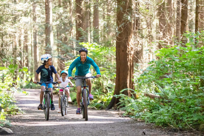 Mother and two young children riding bikes in nature.