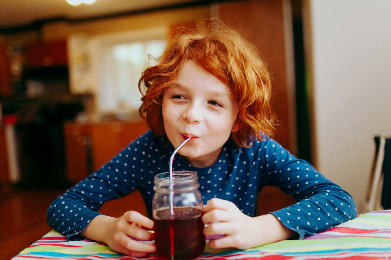Young child drinking cranberry juice in kitchen.
