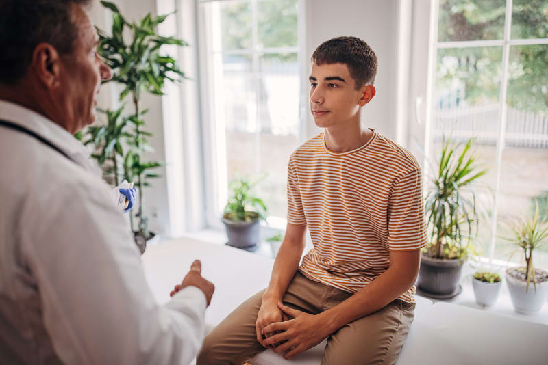 Teenage boy speaking with male doctor at wellness exam.