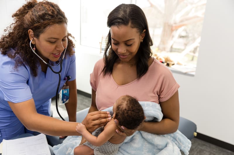 Mother holding Baby while Doctor listens to heart with stethoscope. 
