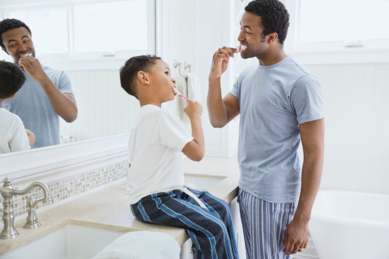 Father and young son brushing teeth together. 