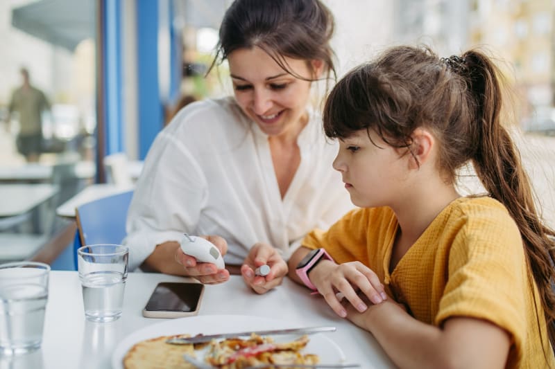 Mother and Daughter checking glucose levels at dinner table.