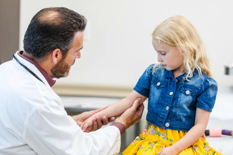 Male doctor examining young girl's elbow.