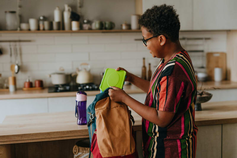 Teenage boy putting lunchbox in his backpack. 