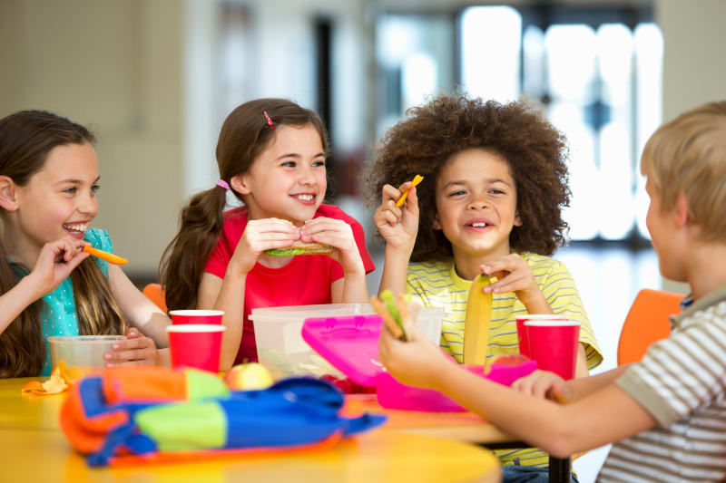 Group of school age children eating lunch in cafeteria.