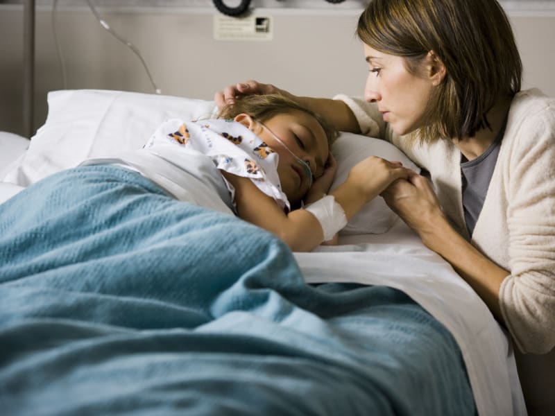 Mother at bedside of resting Child in hospital.