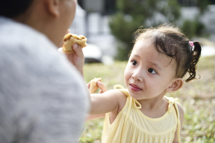Child feeds her parent a bite of sandwich 