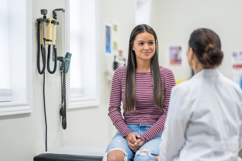 Teenager girl speaking with female doctor at wellness exam.