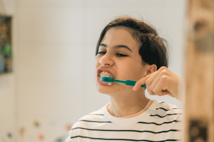 Teenage girl with braces brushing her teeth with a green toothbrush 