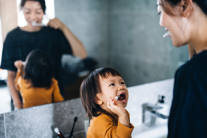 Parent and child brushing teeth in bathroom with toothpaste and water