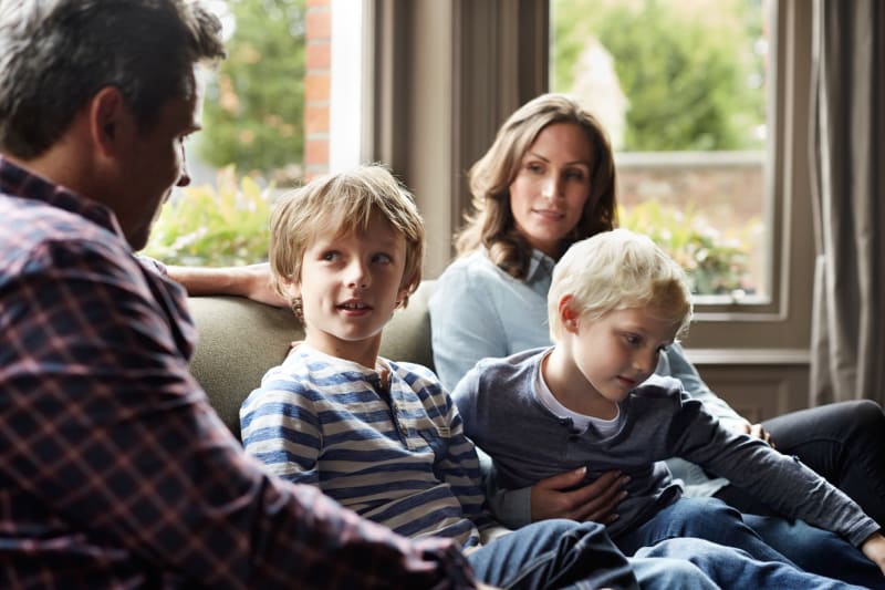 Parents sitting on couch talking with two young sons. 