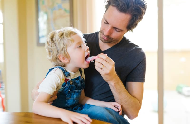 Dad giving young son liquid antibiotic medication.