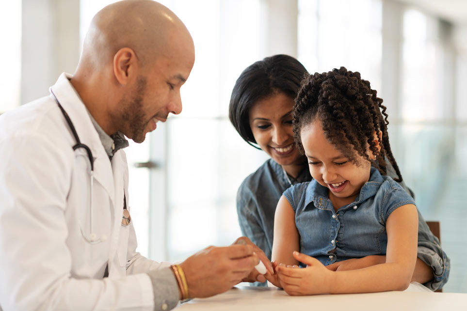 A doctor shows a young girl and her mother how to use an insulin pen.