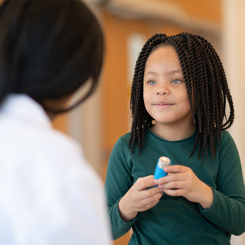 African American girl holding an inhaler talks to her doctor.