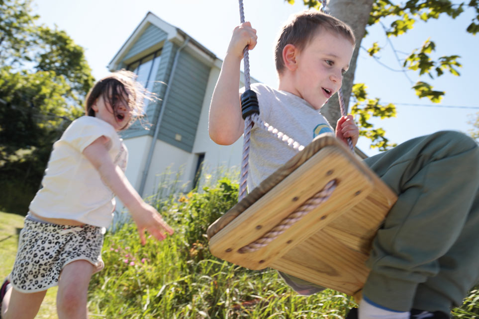 Young children play on swing behind a house.