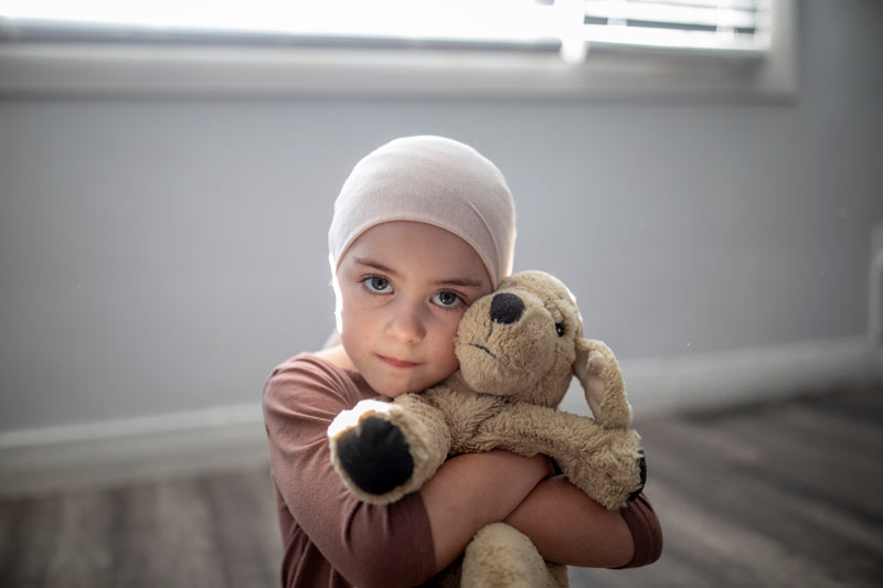 A sweet young girl with cancer, sits on her bedroom floor in the comfort of her own home
