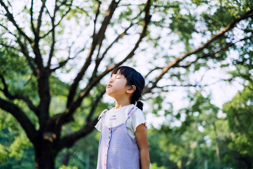 Lovely little Asian girl breathing fresh air with eyes closed in the nature.