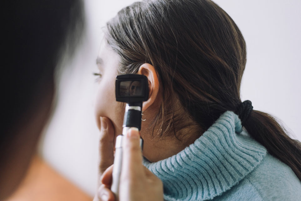 Doctor examining young girl's ear using Otoscope at hospital.