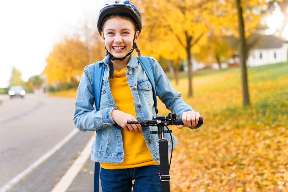 Smiling pre-teen girl wearing a helmet on a scooter