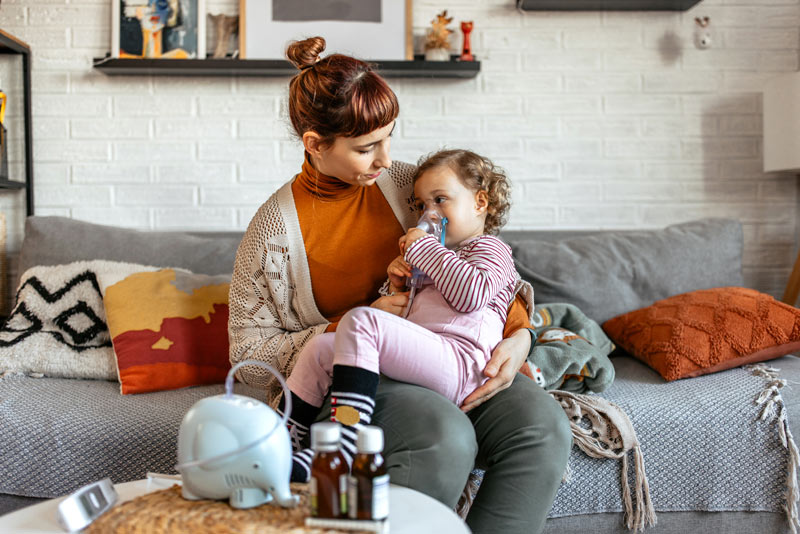 Mother helping her little daughter doing inhalation with a nebulizer.