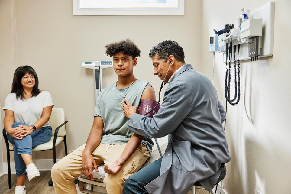 A doctor listens to a young patient's heart in exam room.