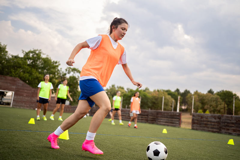 Caucasian teenage girl, a soccer player, dribbling the soccer ball between the sports cones.