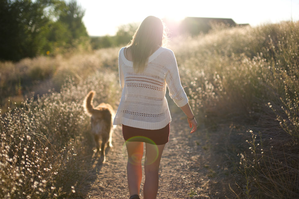 Rear view of a teen girl walking her dog outside.