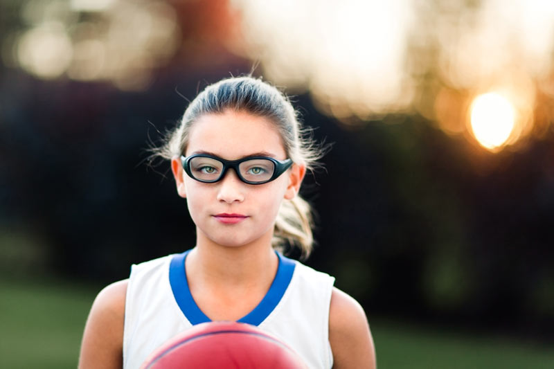 Young girl wearing sports goggles holding a basketball.