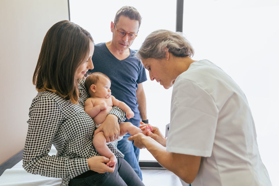 Female doctor examining baby boy with parents at hospital.