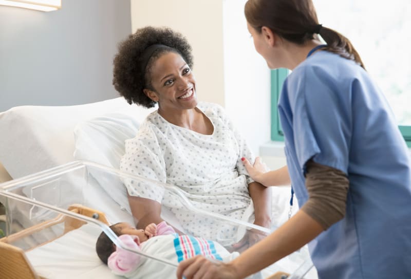 Nurse comforting mother with newborn at hospital.