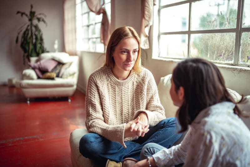 Mother and teenage daughter sitting on couch having a caring discussion.