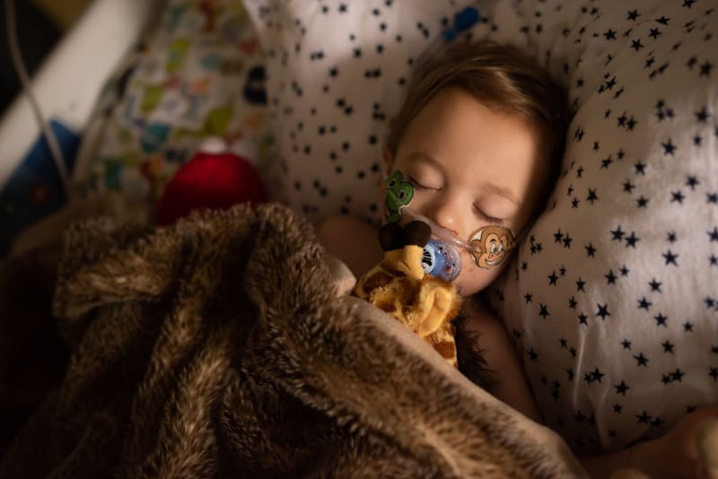 Toddler in hospital pediatric intensive care unit sleeping peacefully with pillow and blankets. 