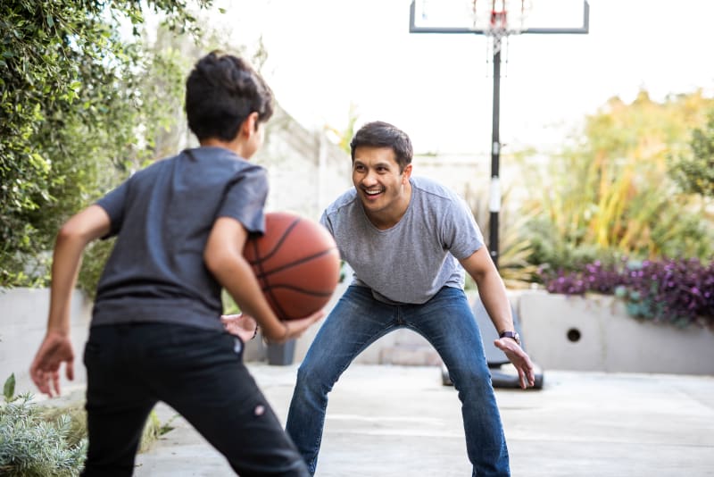 Small teenage boy playing basketball with father. 