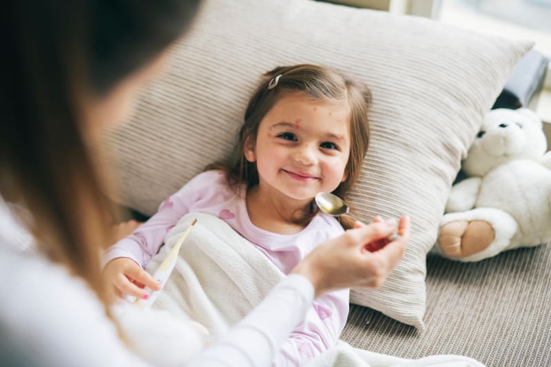 Young girl with chicken pox laying down on couch with mother. 