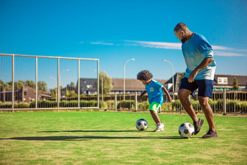 Young boy playing soccer with his father outdoors. 