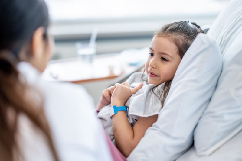 Young girl sitting in hospital bed looking at doctor.