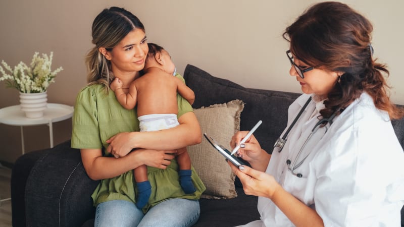 Young woman holding baby while speaking to doctor. 