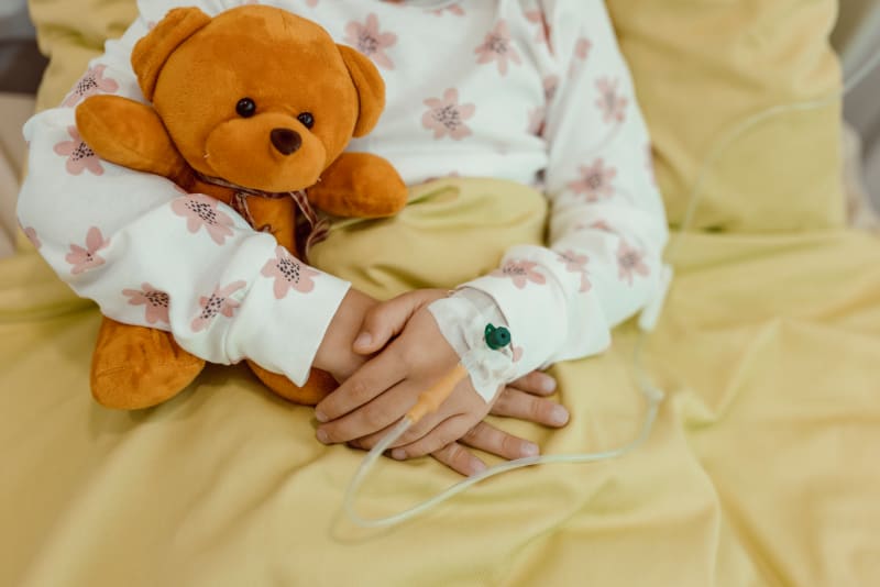 Close up of child's arms wrapped around a teddy bear while receiving medicine through IV. 