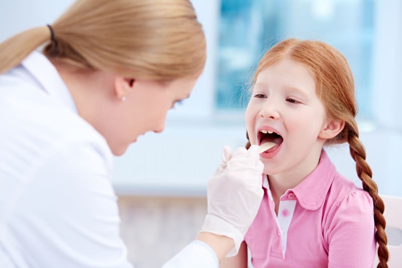 Doctor examining child's throat at clinic.