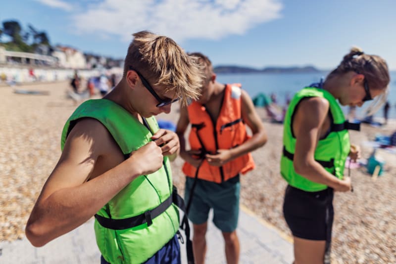 Group of teenagers putting on life vests at the beach. 