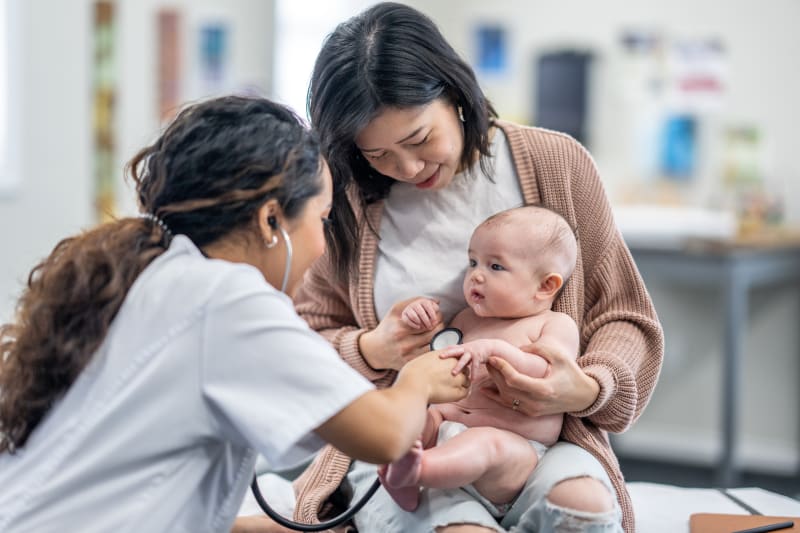 Mother holding her baby while doctor listens to baby's lungs with stethoscope. 