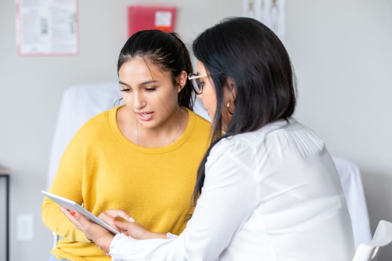 Teenage girl looking at tablet with her doctor at medical appointment.