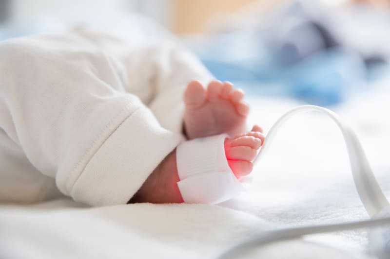 Newborn baby in incubator wearing pulse oximeter on foot. 