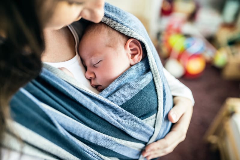 Mother holding infant in wearable swaddle. 