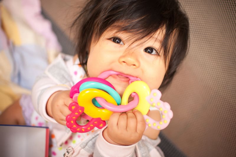 A baby teething on plastic toy.