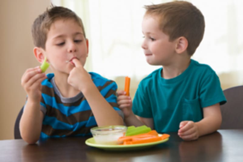 Two young Brothers eating vegetables at the dinner table.